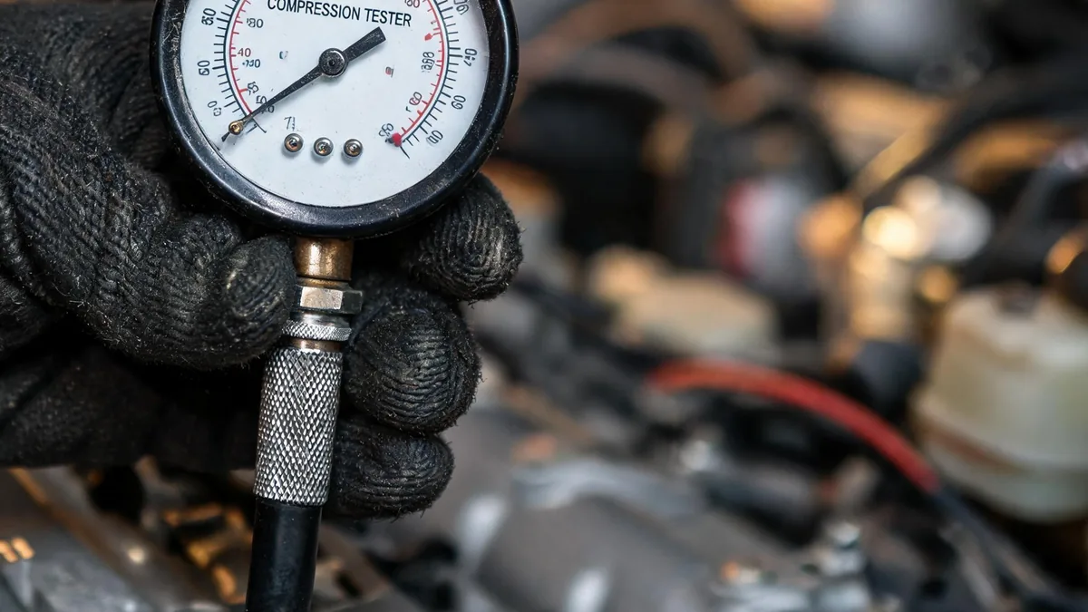 Mechanic performing a compression test on an engine head with an analog gauge, part of the A2Z multi-point inspection