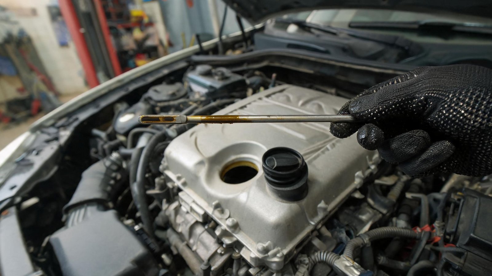 Gloved hand checking engine oil level on a dipstick beside an open oil filler cap